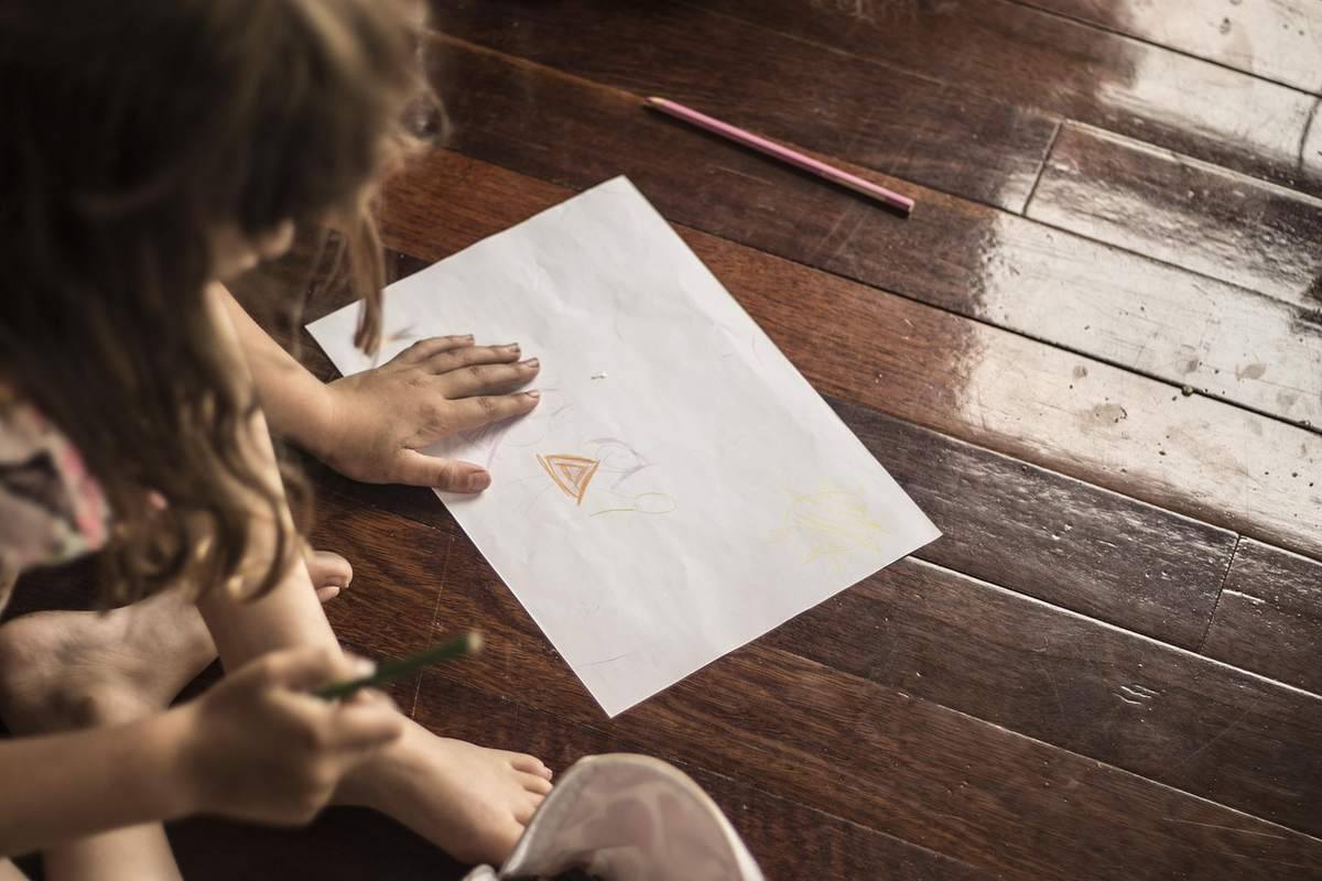 Une fillette dessine un triangle orange sur papier blanc Une fillette dessine un triangle orange sur papier blanc