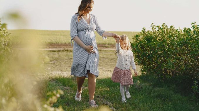 Une femme enceinte marche avec sa fille dans un champ verdoyant