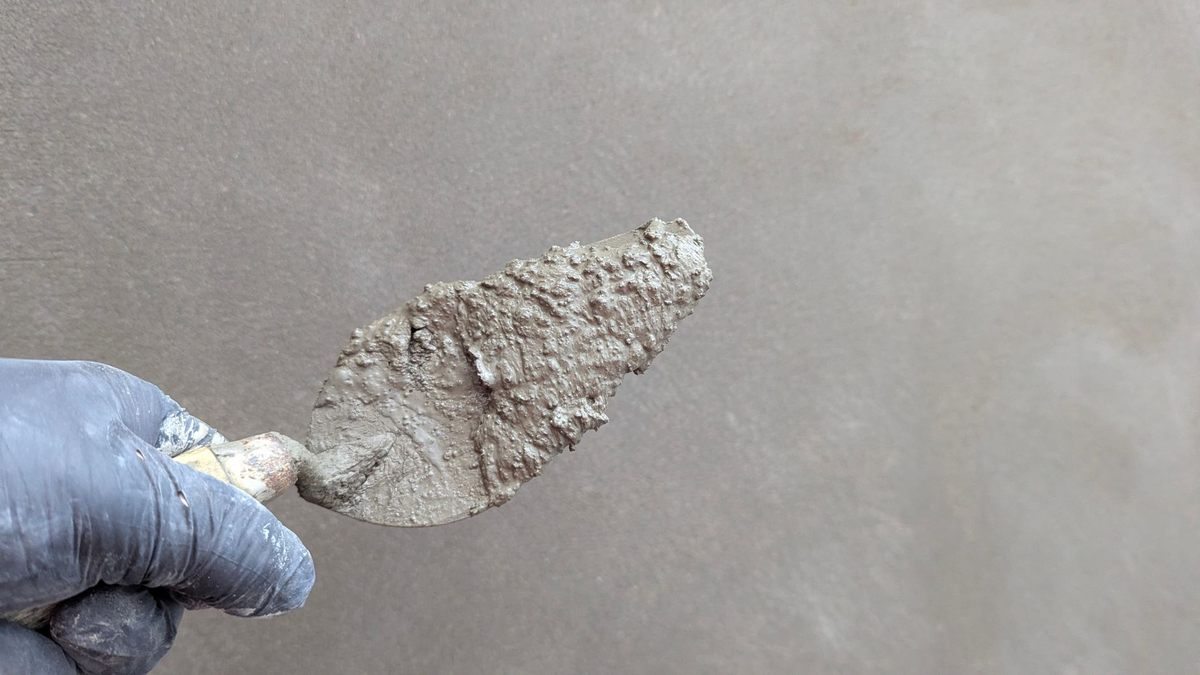 Une main gantée tient une spatule chargée de mortier sur un mur Une main gantée tient une spatule chargée de mortier sur un mur