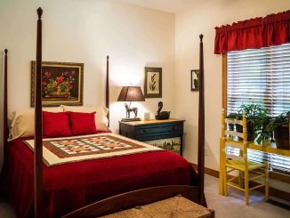 Chambre meublée avec lit à colonnes en bois, couvre-lit rouge et mobilier traditionnel, fenêtre avec rideau rouge