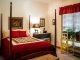 Chambre meublée avec lit à colonnes en bois, couvre-lit rouge et mobilier traditionnel, fenêtre avec rideau rouge