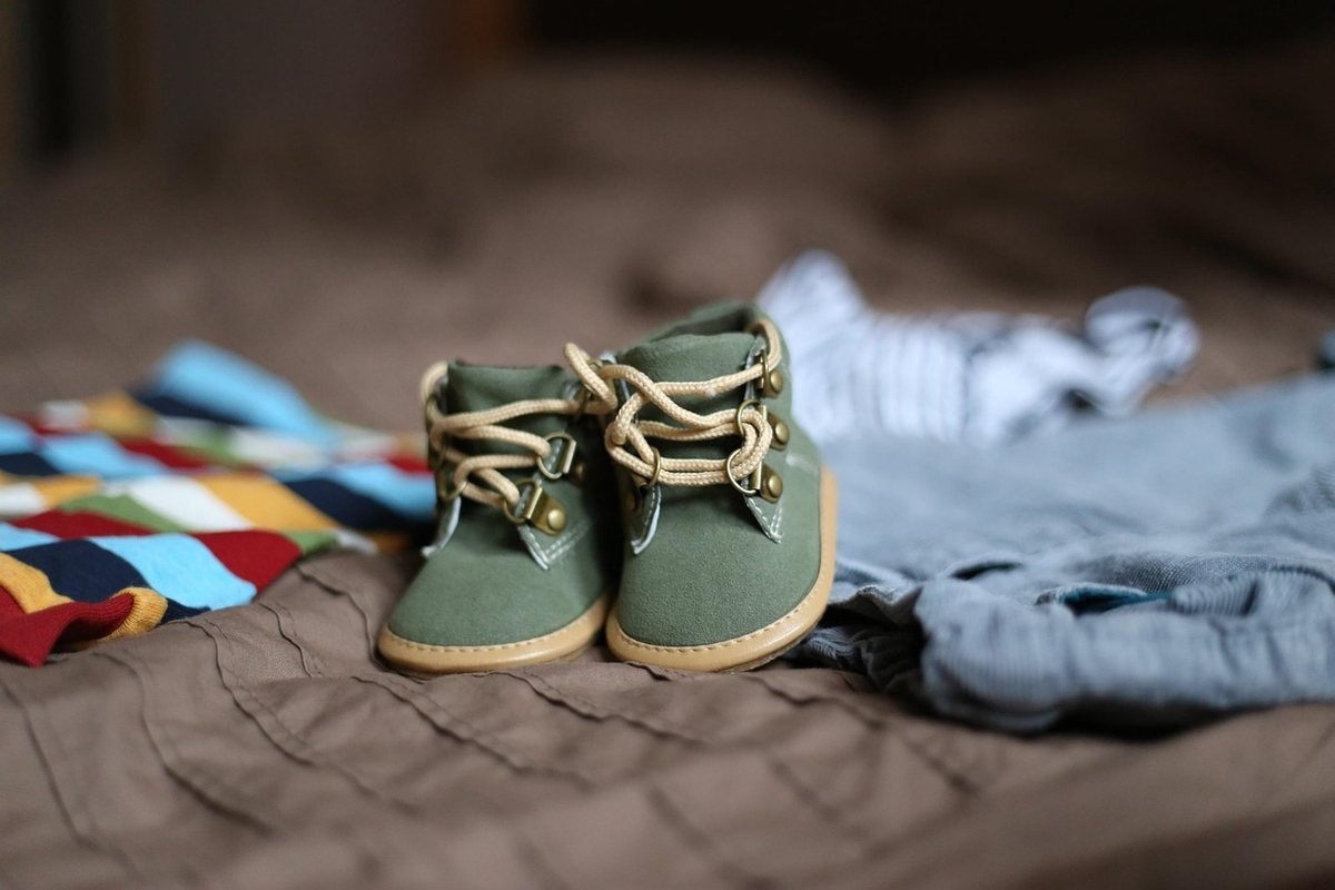 Petites chaussures vertes et vêtements disposés sur un lit doux Petites chaussures vertes et vêtements disposés sur un lit doux