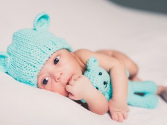 Un nourrisson avec bonnet d'ours et peluche bleue sur drap blanc