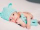 Un nourrisson avec bonnet d'ours et peluche bleue sur drap blanc