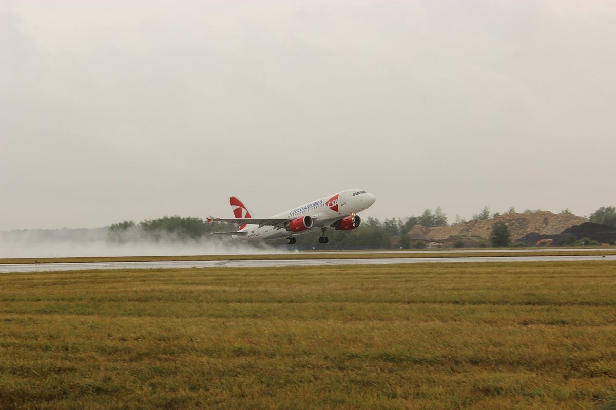 ALT: Un avion rouge et blanc décolle sur une piste mouillée sous ciel gris ALT: Un avion rouge et blanc décolle sur une piste mouillée sous ciel gris