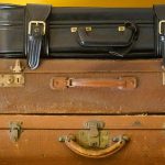Trois valises vintages empilées en cuir marron et noir sur fond jaune