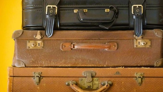 Trois valises vintages empilées en cuir marron et noir sur fond jaune