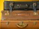 Trois valises vintages empilées en cuir marron et noir sur fond jaune